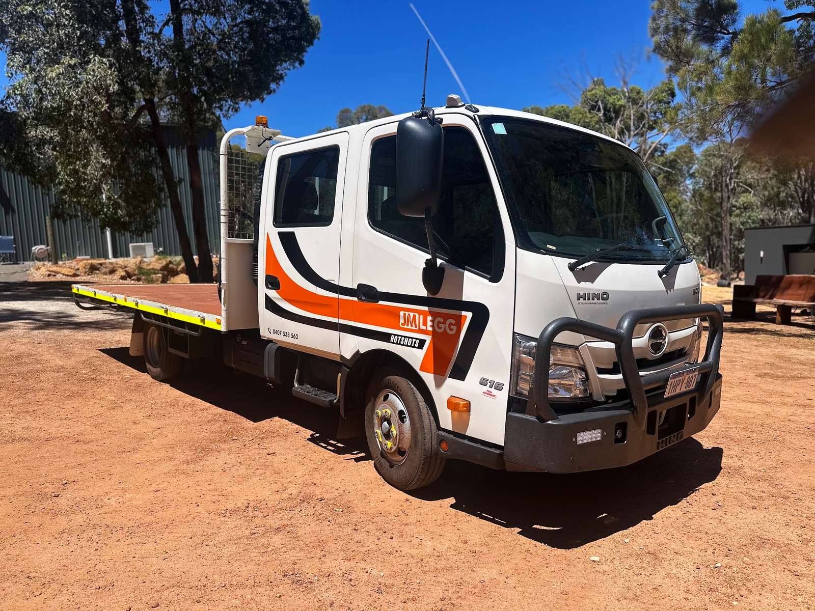 JM Legg Hotshots Hino crew-cab truck with an alloy tray, parked on red dirt in Western Australia