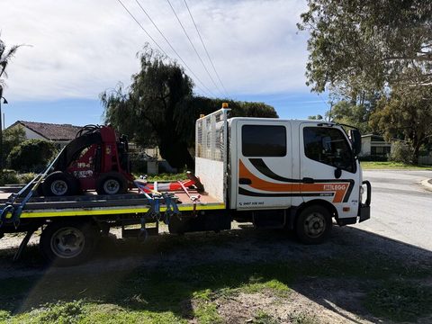 A red mini loader chained down on the JM Legg Hotshots tray, side-on in a suburban street