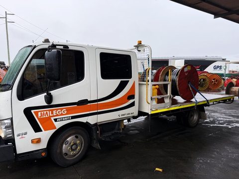 Cable reels strapped down on the JM Legg Hotshots tray at a wet yard, cab and door badge in frame